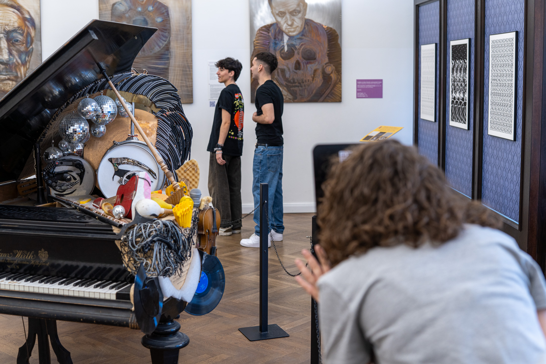 Grand piano sculpture of a face, visitors viewing portraits