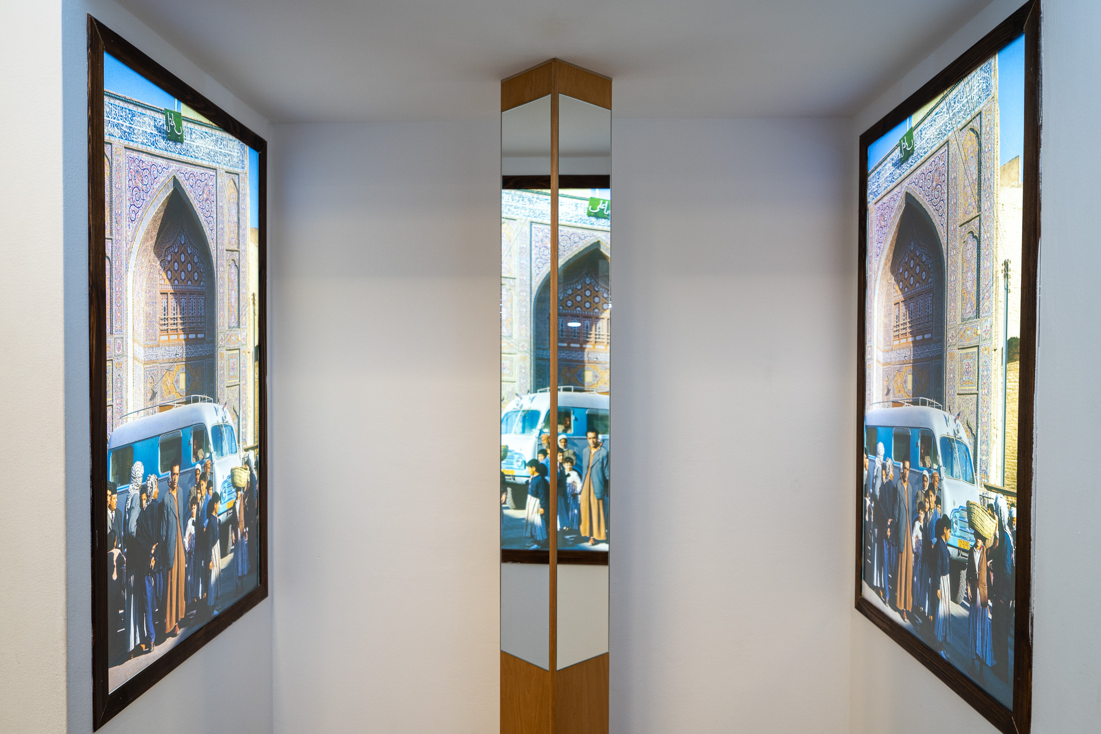 Mirrored column seems to join two framed photos of a mosque gateway