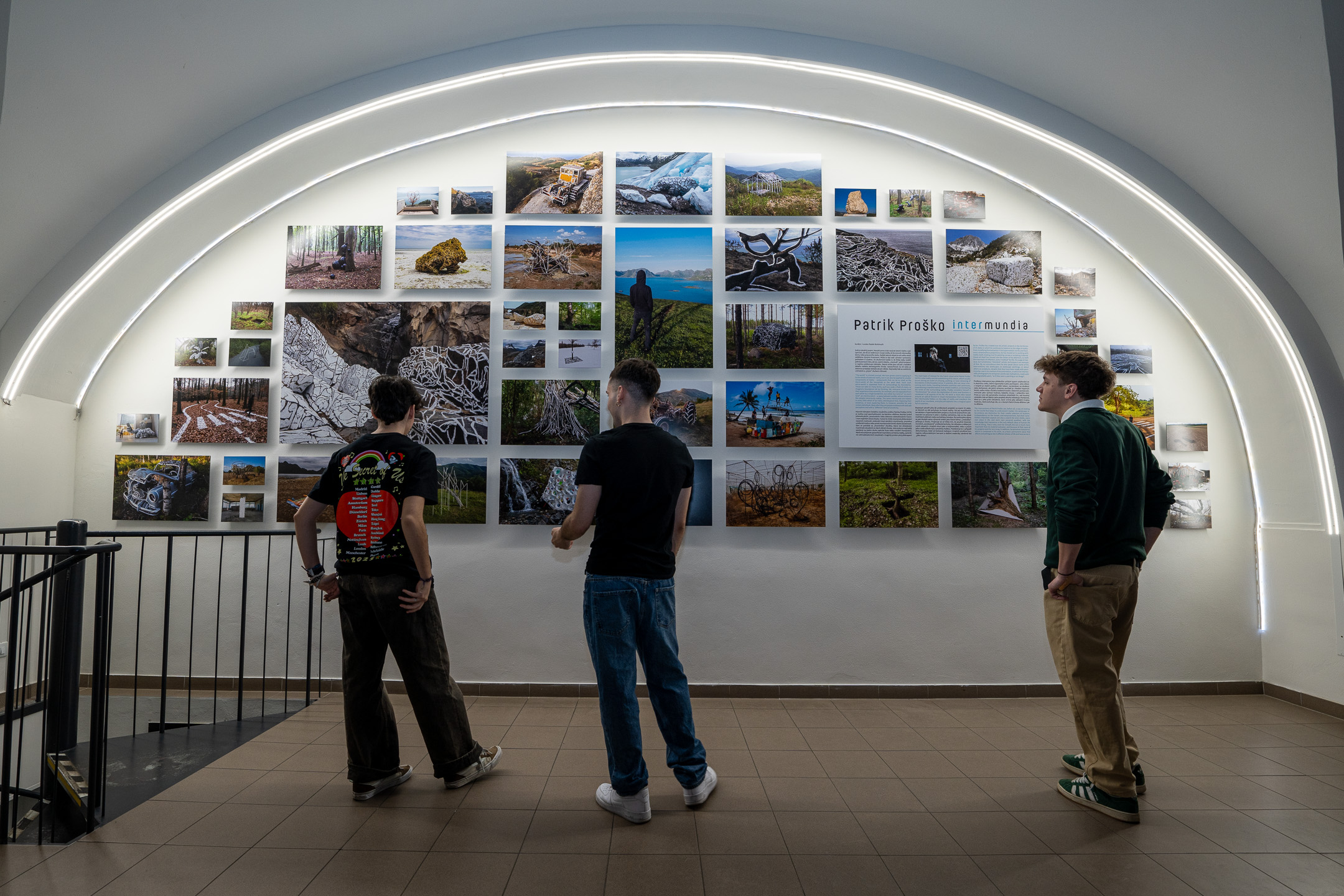 Three visitors view Patrik Proško's Intermundia photo wall under a lit arch