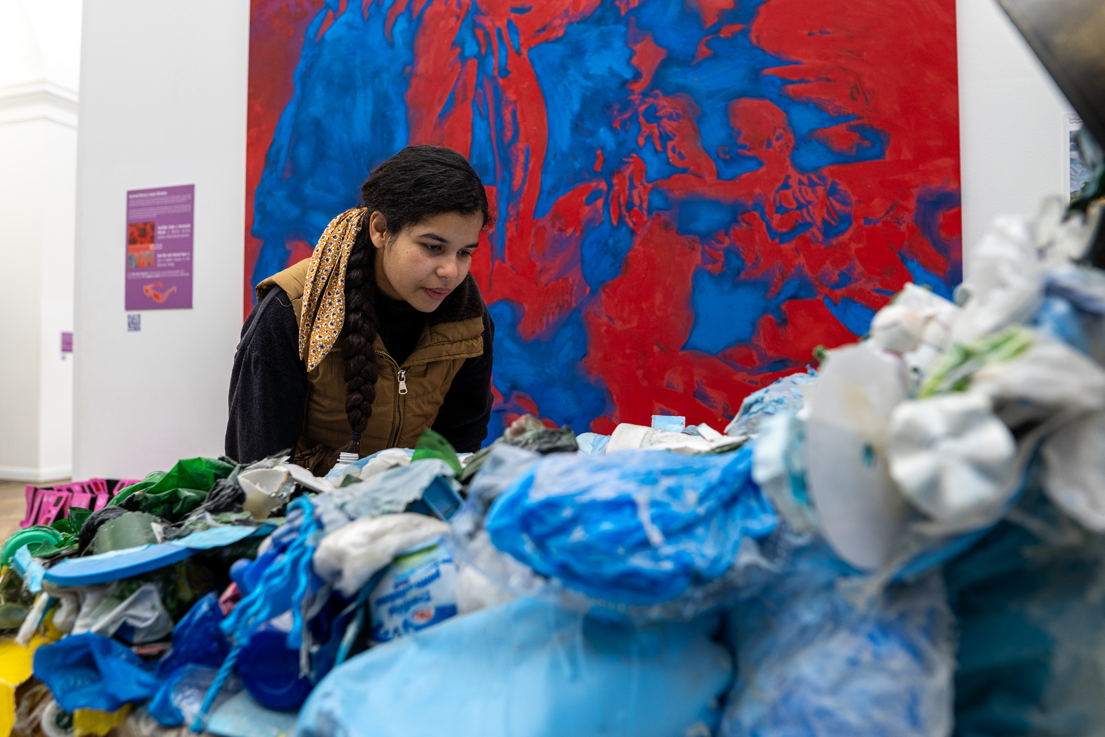 Visitor looks at a plastic waste sculpture beside a red-blue painting