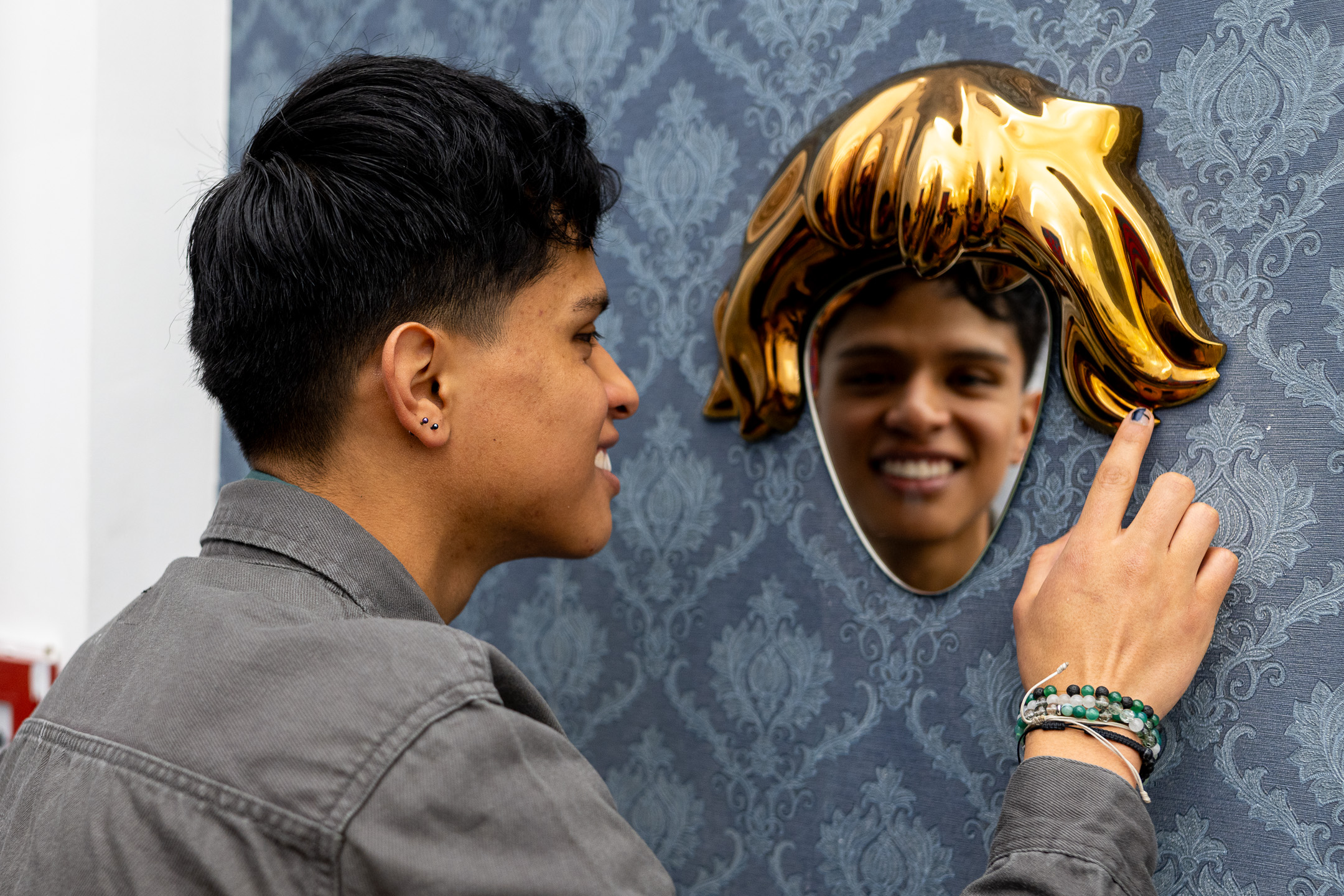 Smiling visitor sees his face in a mirror framed by golden hair