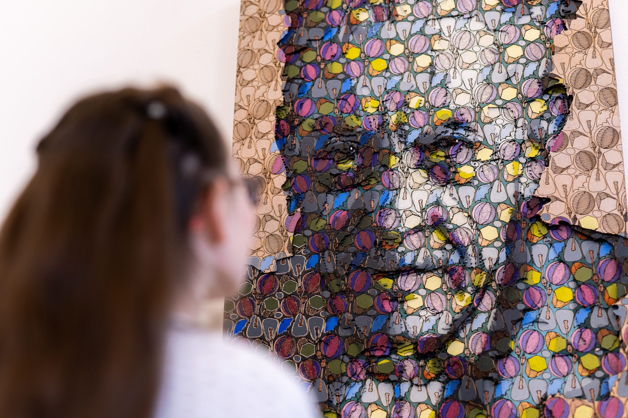 Visitor studies a colourful layered relief portrait of repeating patterns