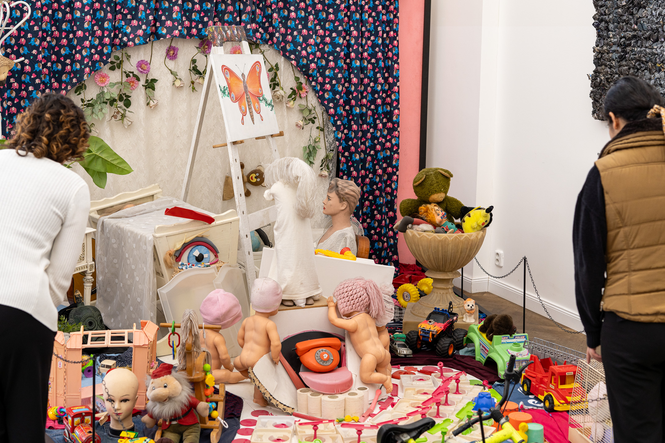 Visitors look at an installation of dolls, toys and a butterfly painting