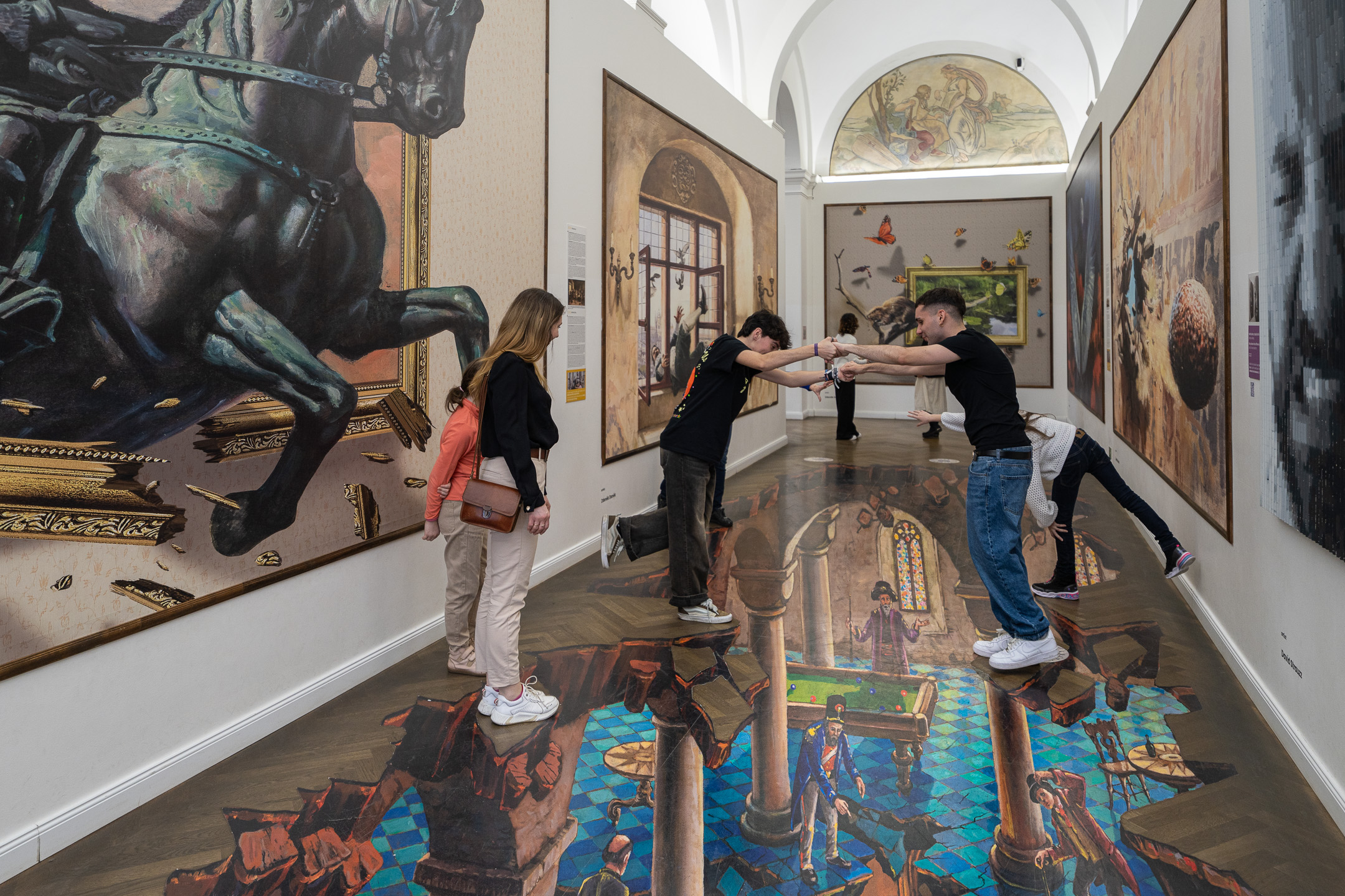 Visitors pose on a 3D floor painting showing a hall below