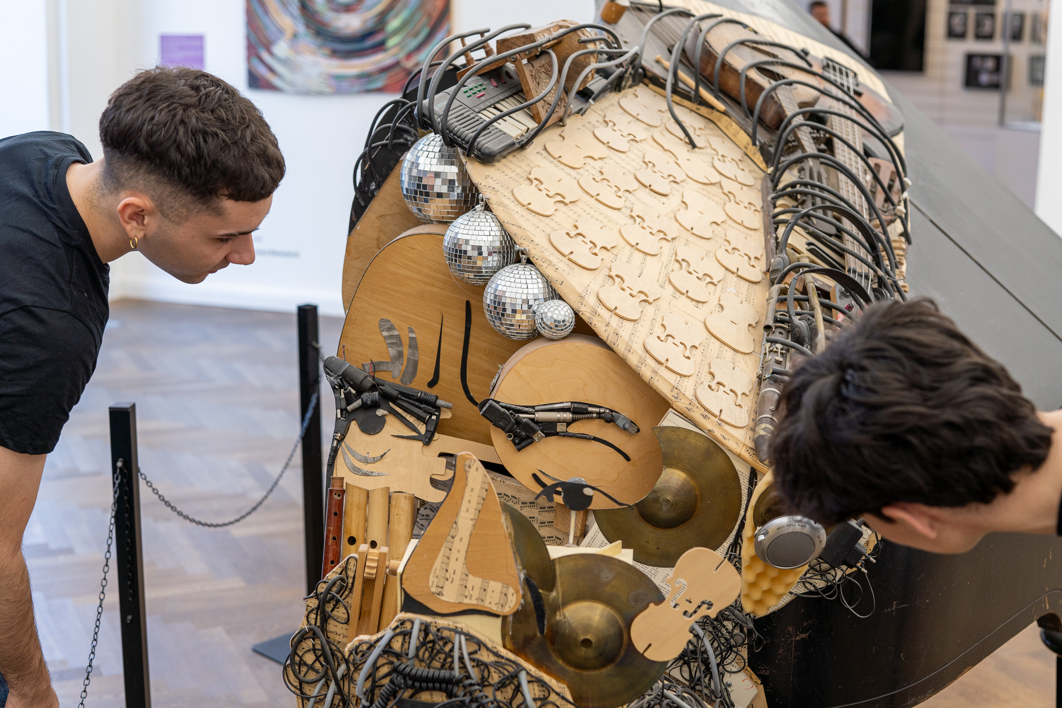 Two young men inspect a face sculpture made of instruments
